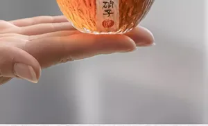 Makro-Detailaufnahme einer japanischen Teetasse aus Hammerschlagglas mit bernsteinfarbenem Tee