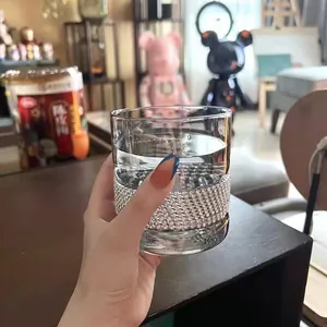 Close-up of luxury glass cup with rhinestone band held in hand in a home setting