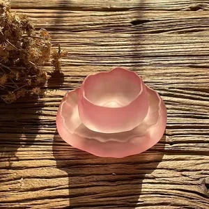 Detailed macro shot of a pink frosted glass tea cup and saucer set on rustic wood surface.