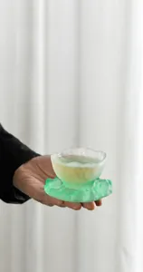 Primer plano de una mano sosteniendo una elegante taza de té de vidrio esmerilado verde