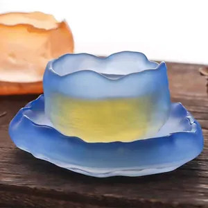 Detail of handcrafted blue frosted glass tea cup with organic wavy rim and saucer.