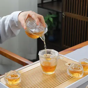 Detailed view of tea being poured from a frosted glass Gaiwan into a matching cup set