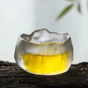 Handmade textured Japanese glass tea cup with irregular rim on dark wood background