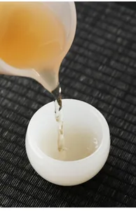 Macro detail of amber tea pouring into a translucent white jade texture tea cup