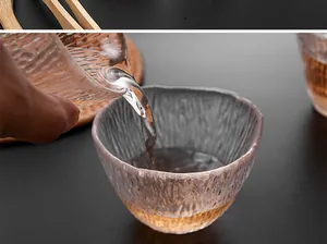 Gros plan de l'eau versée dans une tasse à thé en verre texturé avec dessous de plat