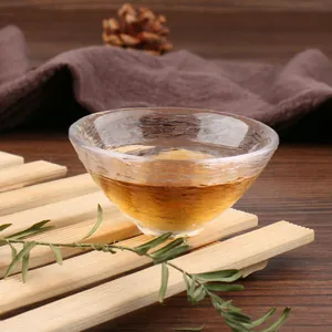 Detailed view of a Japanese style hammered glass tea cup filled with amber tea on wood.