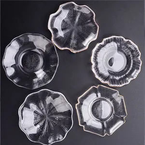 Set aus Glas-Untersetzern mit Goldrand in verschiedenen Blütenformen auf schwarzem Grund.