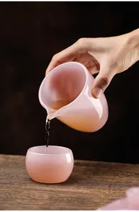 Detailed shot of tea pouring into a translucent pink glass cup on a wooden table.