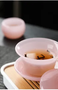 Macro detail of a modern pink translucent glass Gaiwan tea set showing tea texture