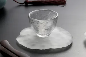 Detailaufnahme einer japanischen Teetasse aus strukturiertem Glas auf einem Untersetzer.