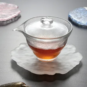 Nahaufnahme einer gefrosteten Teeschale aus Glas mit Deckel auf einem Blatt-Untersetzer