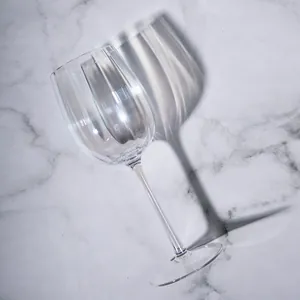 Elegant ribbed crystal Bordeaux wine glass on a minimalist marble background surface.