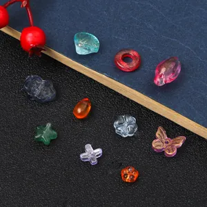 Primer plano detallado de cuentas de vidrio mixtas con formas de mariposa y flor para DIY.