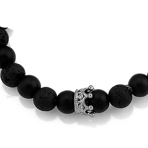 Nahaufnahme eines Armbands aus schwarzen Lavasteinen mit einem silbernen Kronen-Anhänger