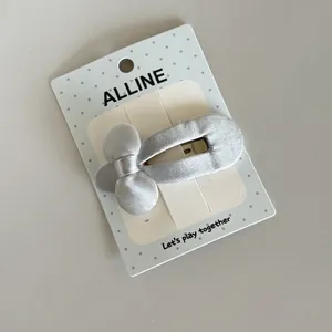 Detailed view of a silver fabric-wrapped bow hair clip on a branded polka-dot card