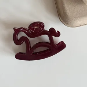 Macro view showing the glossy finish of a dark burgundy rocking horse shaped hair claw clip