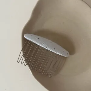 Detail view of a minimalist silver polka dot fabric hair comb on a ceramic plate surface
