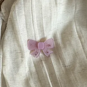 Close-up detail of a pink translucent bow hair clip with tiny rhinestones on fabric