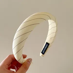 Detalle de una diadema de tela a rayas crema con una etiqueta tejida 'Handmade'.