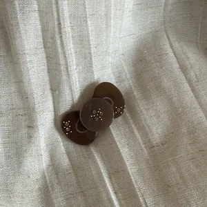 Elegant brown rhinestone bow hair clip detailed view on textured cream fabric background.