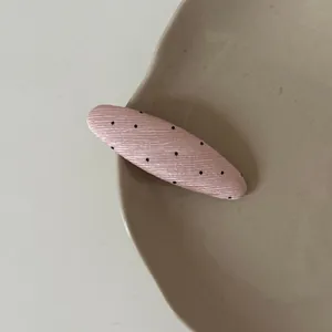 Close-up detail of a pink oval hair clip with black polka dots on a beige ceramic plate