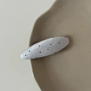 Macro detail of a minimalist white oval hair clip with black polka dots on a plate