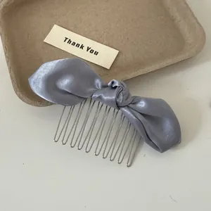 Detail view of a blue satin bow hair comb showing the smooth fabric and metal teeth