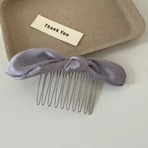 Detail view of a soft purple satin bunny ear bow hair comb on a neutral background tray.