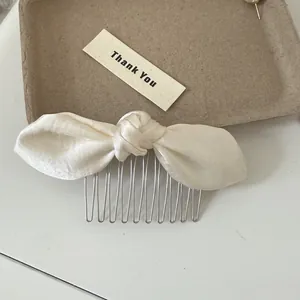 Detailed close-up of a cream-colored satin bow hair comb featuring elegant metal teeth