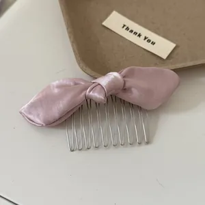 Detailed close-up view of a pink satin bow hair comb with polished metal teeth