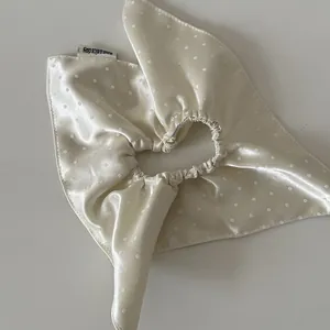 Detailed macro view of cream beige satin polka dot scrunchie scarf texture and sheen