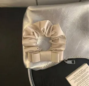 Λεπτομερής άποψη κομψού σατέν scrunchie σε χρώμα σαμπάνιας με φιόγκο σε ασήμι φόντο