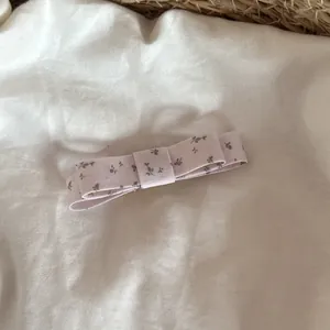 Détail d'une barrette à nœud floral lavande sur un fond de tissu blanc et doux