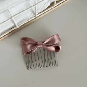 Detail view of a rose pink satin bow hair comb with elegant metallic teeth for styling