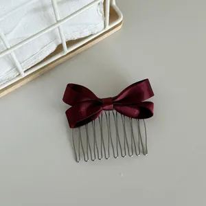 Detailed macro view of an elegant burgundy satin bow hair comb on a neutral background.