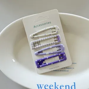 Close-up of four fresh purple and white polka dot and grid hair clips on a card.