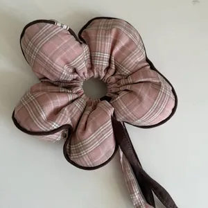 Detailed view of a pink plaid flower-shaped scrunchie hair tie with brown edges