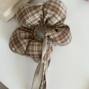Detail showing the brown plaid fabric texture of the flower-shaped scrunchie with ribbons