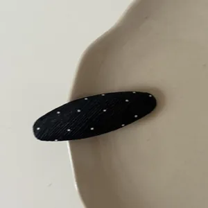Detailed macro view of a black polka dot oval hair clip with ribbed fabric texture.