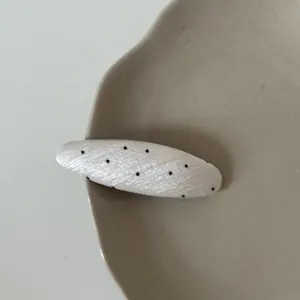 Close-up of a white elliptical hair clip with black polka dots on a beige plate.