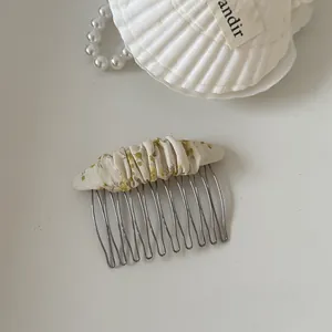 Close-up detail of a cream floral fabric hair comb accessory with silver metal tines