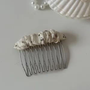 Detailed close-up of a sweet floral fabric hair comb with silver metal teeth on a white surface