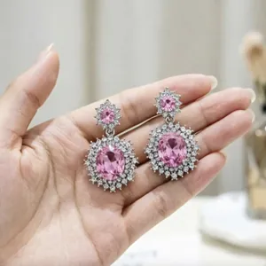 Orecchini pendenti con cristallo rosa e diamanti halo mostrati su una mano in dettaglio