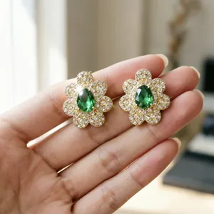 Primo piano di orecchini a fiore in oro con pietre verdi a goccia sulla mano.