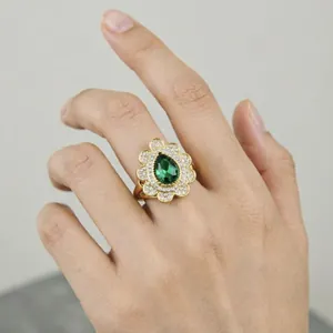 Vista dettagliata di un anello di lusso in oro con gemma verde a goccia e alone floreale.
