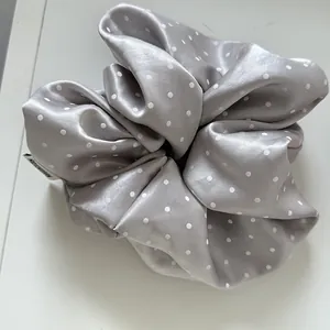 A detailed macro shot of a shiny silver-gray satin scrunchie featuring white polka dots