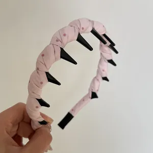 Detailed close-up of pink polka dot fabric headband with black teeth for hair styling.