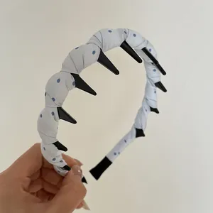 Detailed close-up of a blue polka dot fabric wrapped headband with black plastic long teeth