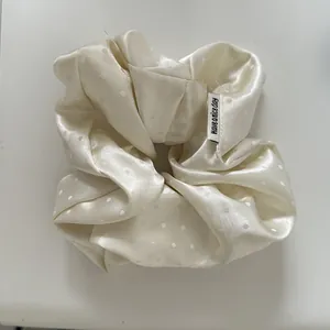 Close-up of a white satin polka dot scrunchie with "Have a nice day" tag detail.