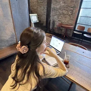 Close-up of a French elegant pink rose hair claw clip worn in a cozy cafe setting.
